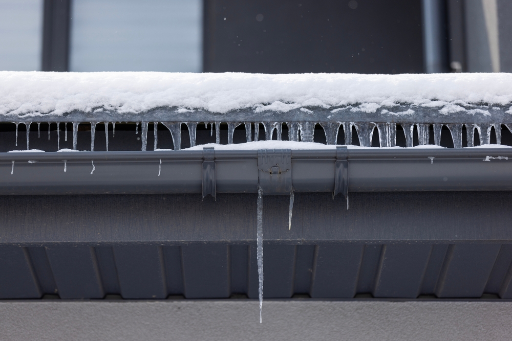 Icicles,hanging,from,a,snow covered,eave,and,black,gutter,on